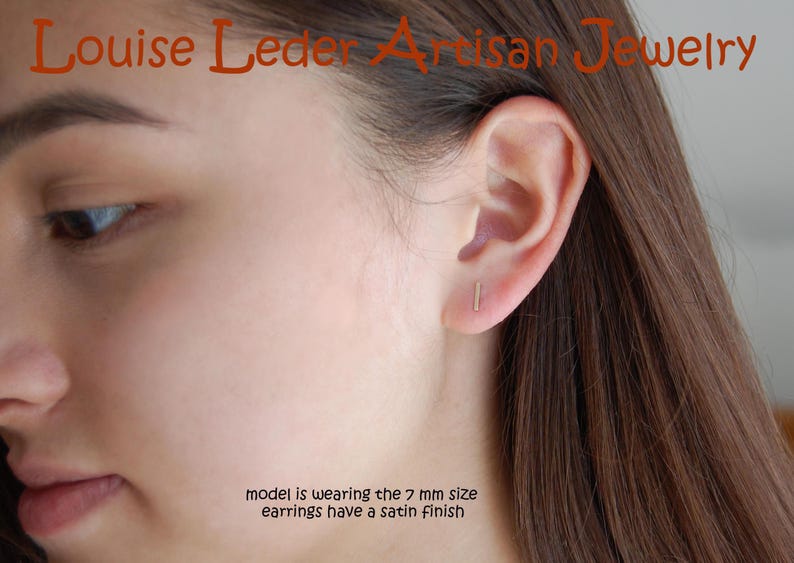 May include: A close-up of a person's face and ear, showcasing a small, gold-colored bar earring. The earrings have a satin finish. The text "Louise Leder Artisan Jewelry" is at the top. The text "model is wearing the 7 mm size earrings have a satin finish" is at the bottom.
