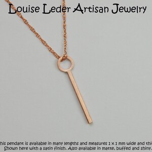 Puede incluir: Collar con colgante de oro rosa de dise&ntilde;o minimalista. El colgante es una barra recta con una parte superior circular, suspendida de una delicada cadena. El colgante mide aproximadamente 1 mm de ancho y grosor. El texto "Louise Leder Artisan Jewelry" est&aacute; arriba.