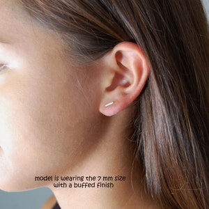 Puede incluir: Primer plano de la oreja de una persona con un peque&ntilde;o pendiente de barra de plata. La modelo lleva la talla de 7 mm con un acabado pulido.