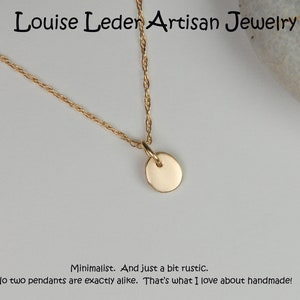 May include: A gold-colored necklace with a small, round pendant. The necklace is displayed on a light background. The text "Louise Leder Artisan Jewelry" is at the top. The text "Minimalist. And just a bit rustic. No two pendants are exactly alike. That's what I love about handmade!" is at the bottom.