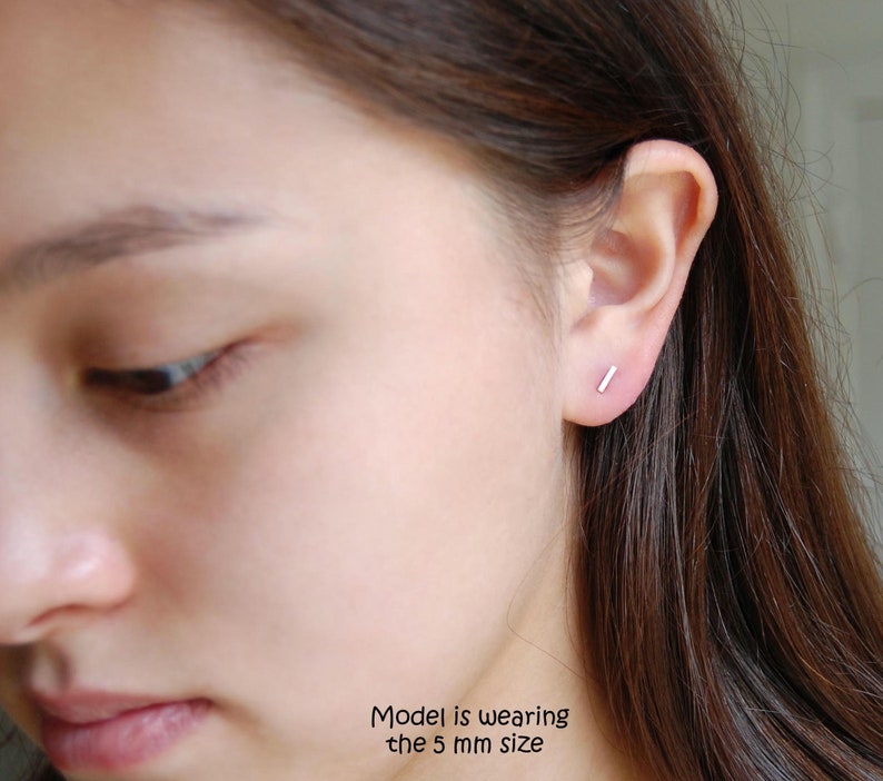 May include: A close-up of a person's ear with a small, silver bar earring. The model is wearing the 5 mm size.