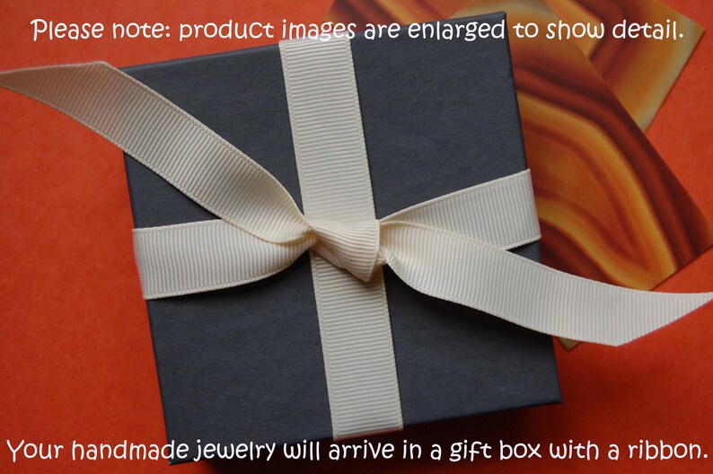 May include: A dark gray gift box tied with a cream-colored ribbon, presented on an orange background. The text at the top says, "Please note: product images are enlarged to show detail." The text at the bottom says, "Your handmade jewelry will arrive in a gift box with a ribbon."