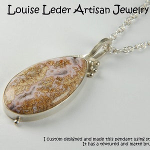 Puede incluir: Un collar de plata con un colgante con acabado texturizado y cepillado mate. El colgante presenta una piedra en forma de l&aacute;grima con patrones de remolino marrones, blancos y rosados.