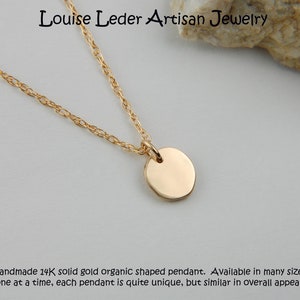 May include: A gold necklace featuring a circular pendant suspended from a fine chain. The image includes the text "Louise Leder Artisan Jewelry". The text at the bottom says "Handmade 14K solid gold organic shaped pendant."