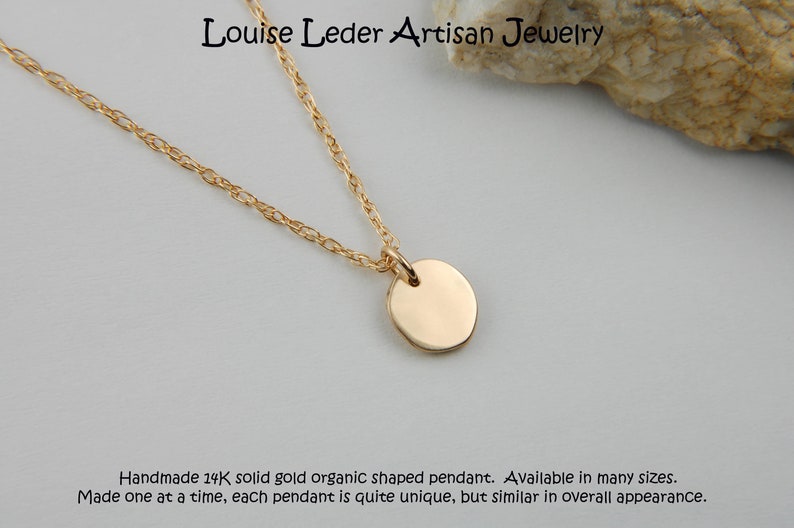 May include: A gold necklace featuring a circular pendant suspended from a fine chain. The image includes the text "Louise Leder Artisan Jewelry". The text at the bottom says "Handmade 14K solid gold organic shaped pendant."