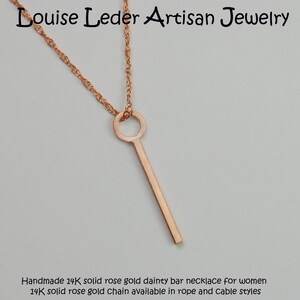Puede incluir: Collar de barra de oro rosa con una cadena delicada. El colgante es una barra vertical delgada suspendida de un bucle circular. La cadena es de estilo cuerda trenzada. El texto "Louise Leder Artisan Jewelry" est&aacute; en la parte superior.