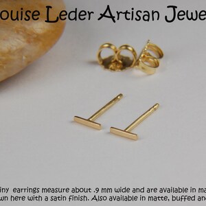 May include: Gold-colored bar stud earrings with a satin finish, displayed with earring backs. The earrings are approximately .9 mm wide. The text "Louise Leder Artisan Jewelry" is at the top, and additional text is at the bottom.