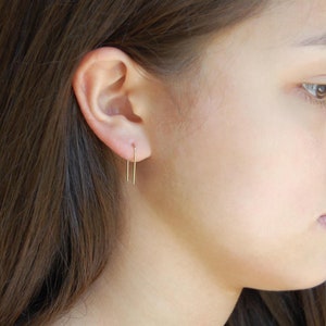 Puede incluir: Primer plano de la oreja de una persona con un par de finos pendientes de barra de oro. Los pendientes son simples y delicados, y son una opci&oacute;n popular para el uso diario.