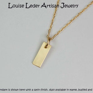 May include: A gold-coloured rectangular pendant necklace with a delicate chain. The pendant is a simple, polished rectangle. The text "Louise Leder Artisan Jewelry" is at the top. The pendant is shown with a satin finish.