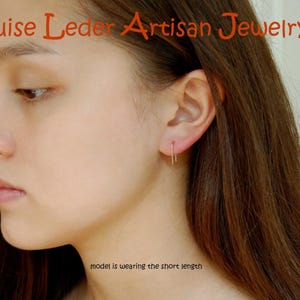 May include: A thin, gold-toned U-shaped earring worn in the earlobe. The text 'Louise Leder Artisan Jewelry' appears at the top, and the text 'model is wearing the short length' is positioned near the bottom of the image.
