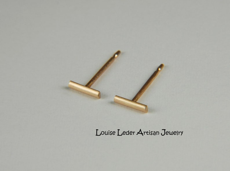 Puede incluir: Un par de pendientes de barra de oro. Los pendientes son simples y minimalistas, con una peque&ntilde;a barra rectangular.