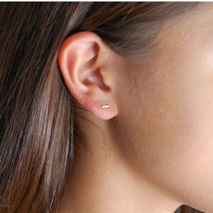 Puede incluir: Primer plano de una oreja con un peque&ntilde;o pendiente de barra de oro delgado.
