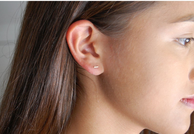 Puede incluir: Primer plano de una oreja con un peque&ntilde;o pendiente de barra de oro delgado.