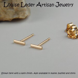 Puede incluir: Un par de pendientes de barra de oro. Los pendientes se muestran con un acabado satinado. El texto "Louise Leder Artisan Jewelry" est&aacute; en la parte superior de la imagen. El texto "Shown here with a satin finish. Also available in matte, buffed and shiny." est&aacute; en la parte inferior de la imagen.