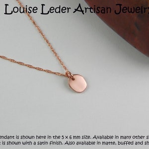 Puede incluir: Collar de oro rosa con un peque&ntilde;o colgante ovalado. El colgante mide aproximadamente 5 x 6 mm y cuelga de una fina cadena. El collar tiene un acabado satinado. El texto en la imagen dice "Louise Leder Artisan Jewelry".