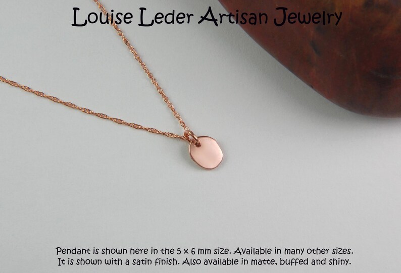 Puede incluir: Collar de oro rosa con un peque&ntilde;o colgante ovalado. El colgante mide aproximadamente 5 x 6 mm y cuelga de una fina cadena. El collar tiene un acabado satinado. El texto en la imagen dice "Louise Leder Artisan Jewelry".