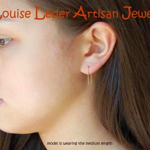 May include: A gold-toned U-shaped wire earring worn in the earlobe. The text 'Louise Leder Artisan Jewelry' appears at the top, and the text 'model is wearing the medium length' is positioned at the bottom of the image.