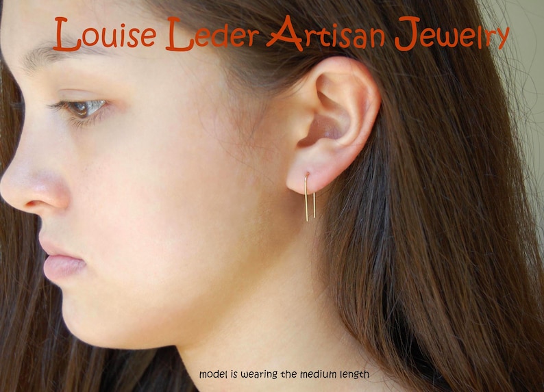 May include: A gold-toned U-shaped wire earring worn in the earlobe. The text 'Louise Leder Artisan Jewelry' appears at the top, and the text 'model is wearing the medium length' is positioned at the bottom of the image.