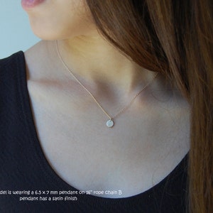 May include: A delicate gold necklace with a small, round pendant. The pendant, approximately 6.5 x 7 mm, hangs from a thin chain. The necklace has a satin finish. The model is wearing a 40.6 cm rope chain.