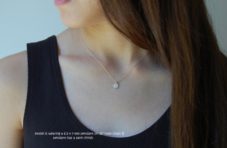 May include: A delicate gold necklace with a small, round pendant. The pendant, approximately 6.5 x 7 mm, hangs from a thin chain. The necklace has a satin finish. The model is wearing a 40.6 cm rope chain.