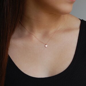 Puede incluir: Un delicado collar de oro rosa con un peque&ntilde;o colgante redondo. El colgante cuelga de una fina cadena, creando un look minimalista y elegante. El collar se lleva sobre una camiseta negra, resaltando su sutil brillo.