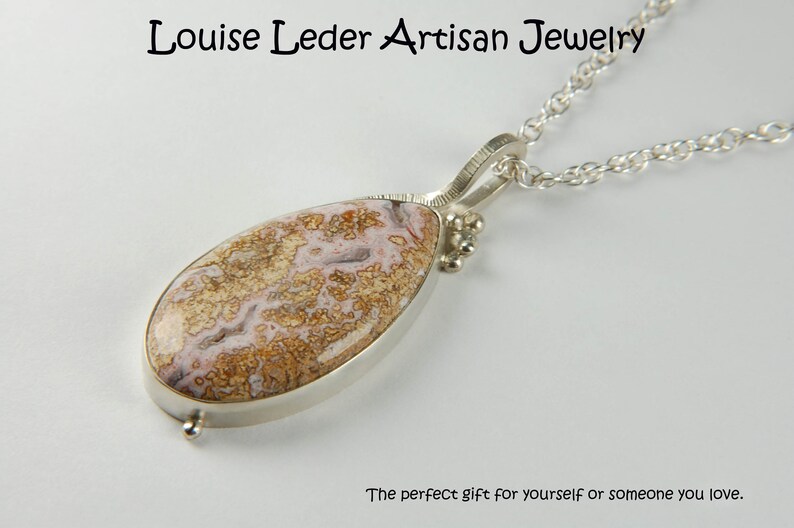 Puede incluir: Un collar de cadena de plata con un colgante en forma de l&aacute;grima con una piedra de &aacute;gata marr&oacute;n y rosa.