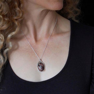 May include: A silver chain necklace with a pendant featuring a brown and white oval stone.