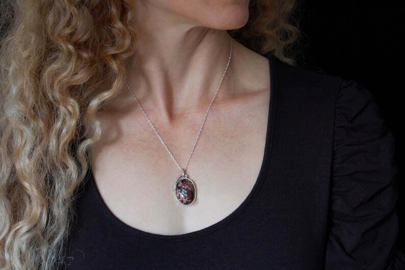 May include: A silver chain necklace with a pendant featuring a brown and white oval stone.