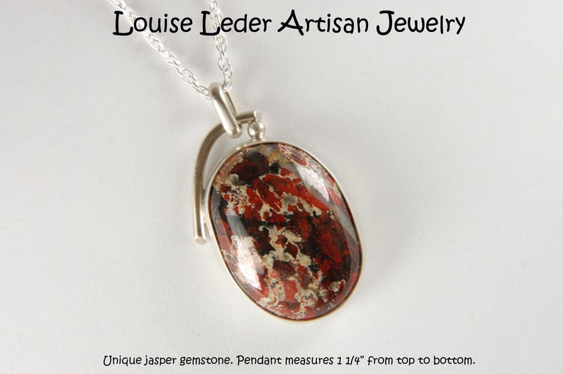 May include: A silver pendant with a unique jasper gemstone. The gemstone is red, black, and white with a swirling pattern. The pendant measures 1 1/4 inches from top to bottom.