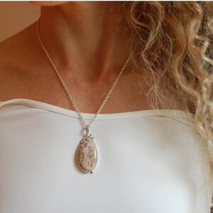Puede incluir: Un collar de cadena de plata con un colgante con una piedra ovalada de color marr&oacute;n claro y blanco.