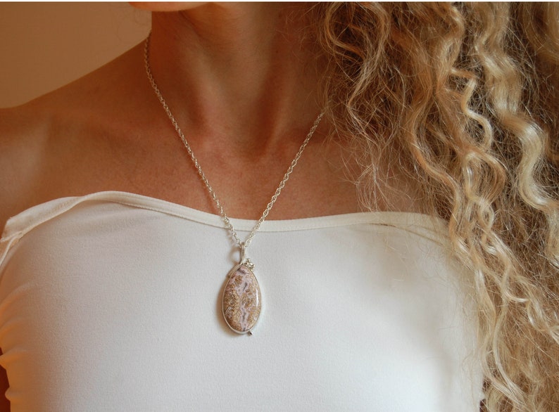 Puede incluir: Un collar de cadena de plata con un colgante con una piedra ovalada de color marr&oacute;n claro y blanco.