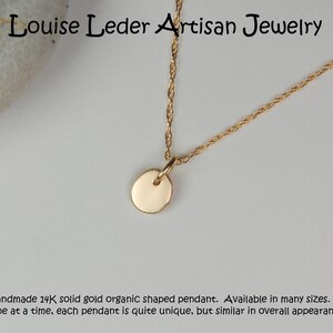 May include: A gold-colored necklace with a small, round pendant. The pendant hangs from a delicate chain. The text "Louise Leder Artisan Jewelry" is at the top. The description says "Handmade 14K solid gold organic shaped pendant."