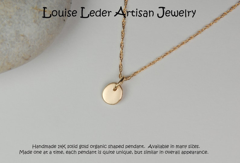 May include: A gold-colored necklace with a small, round pendant. The pendant hangs from a delicate chain. The text "Louise Leder Artisan Jewelry" is at the top. The description says "Handmade 14K solid gold organic shaped pendant."