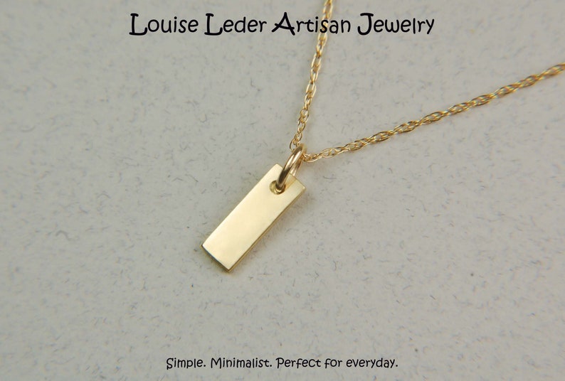 May include: A gold-coloured rectangular pendant necklace. The pendant hangs from a delicate chain. The text "Louise Leder Artisan Jewelry" is at the top of the image. The text "Simple. Minimalist. Perfect for everyday." is at the bottom.