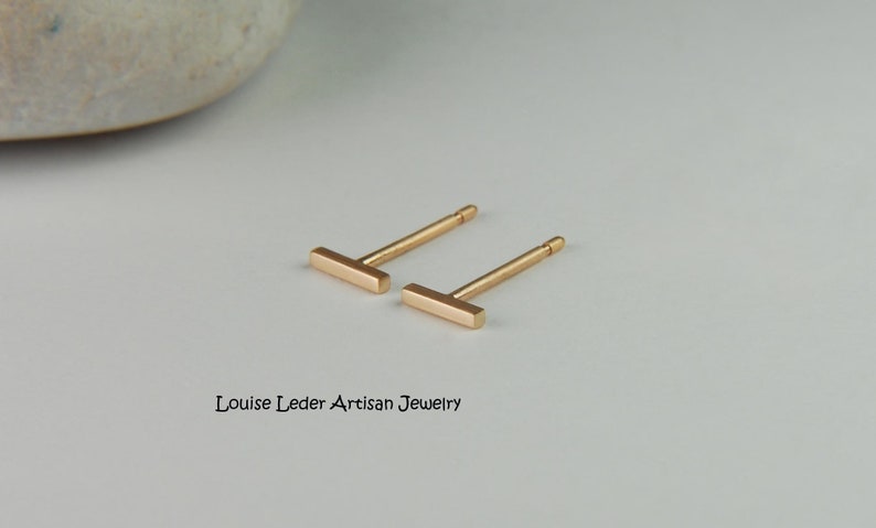 May include: A pair of gold bar stud earrings. The earrings are simple and minimalist, with a straight bar design.