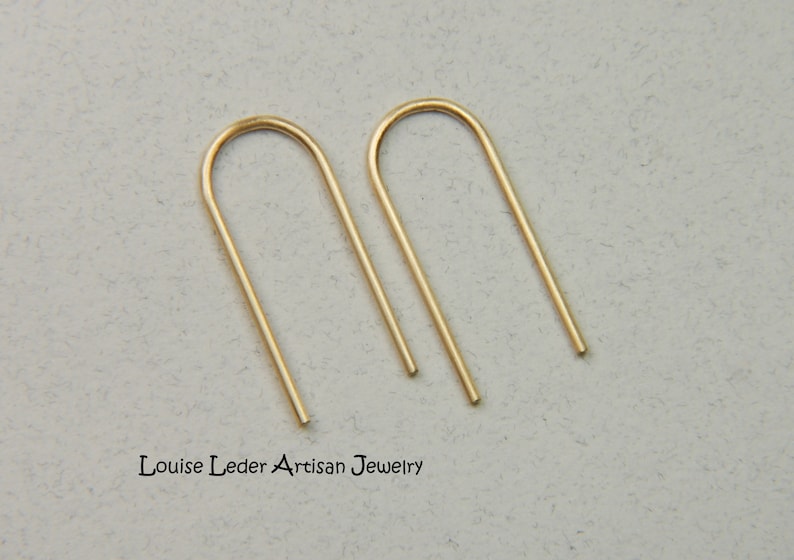Puede incluir: Un par de pendientes de aro abierto minimalistas de color dorado. Los pendientes est&aacute;n hechos de metal fino y liso y tienen un dise&ntilde;o simple y moderno.