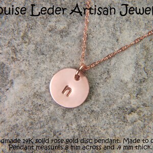 May include: A rose gold necklace featuring a small circular disc pendant stamped with the lowercase letter n. The pendant is suspended from a delicate rose gold chain. Text on the image reads Louise Leder Artisan Jewelry and Handmade 14K solid rose gold disc pendant. Made to order. Pendant measures 8 mm across and .4 mm thick.