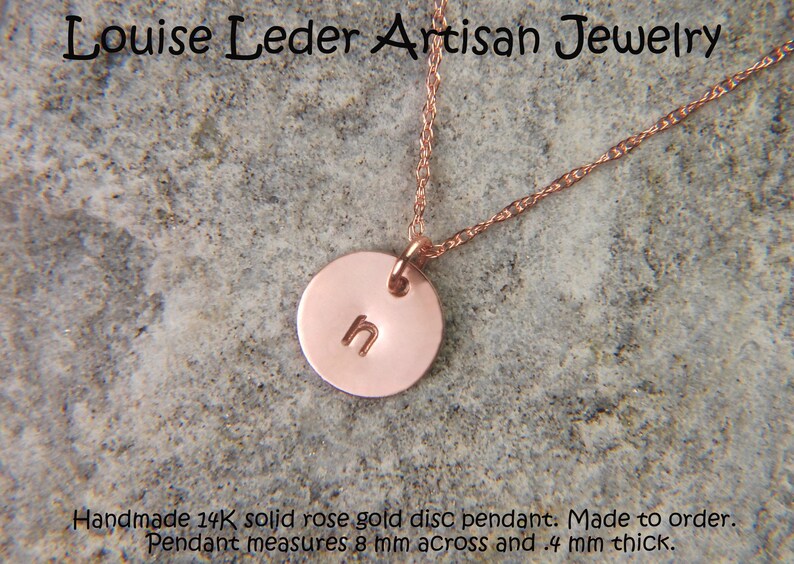 May include: A rose gold necklace featuring a small circular disc pendant stamped with the lowercase letter n. The pendant is suspended from a delicate rose gold chain. Text on the image reads Louise Leder Artisan Jewelry and Handmade 14K solid rose gold disc pendant. Made to order. Pendant measures 8 mm across and .4 mm thick.