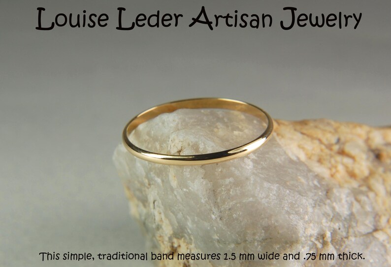 May include: A gold-coloured ring band resting on a textured stone. The text at the top reads Louise Leder Artisan Jewelry, and the text at the bottom reads This simple, traditional band measures 1.5 mm wide and .75 mm thick. The ring is smooth.