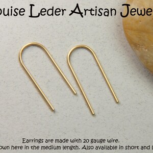 May include: A pair of gold-toned U-shaped wire earrings. The text reads: Louise Leder Artisan Jewelry. Earrings are made with 20 gauge wire. Shown here in the medium length. Also available in short and long.
