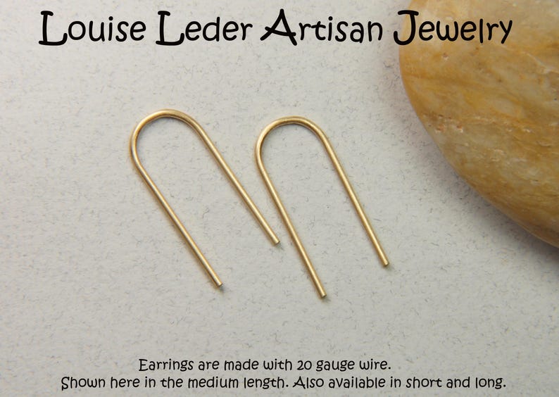 May include: A pair of gold-toned U-shaped wire earrings. The text reads: Louise Leder Artisan Jewelry. Earrings are made with 20 gauge wire. Shown here in the medium length. Also available in short and long.