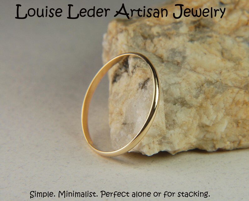 May include: A thin, polished gold band ring with a smooth, rounded surface. The text 'Louise Leder Artisan Jewelry' appears at the top, and the text 'Simple. Minimalist. Perfect alone or for stacking.' appears at the bottom of the image.