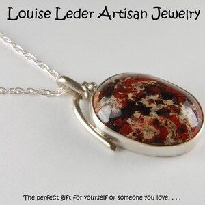 May include: A silver necklace with a red, black, and white patterned oval pendant. The pendant is set in a silver frame and hangs from a silver chain.
