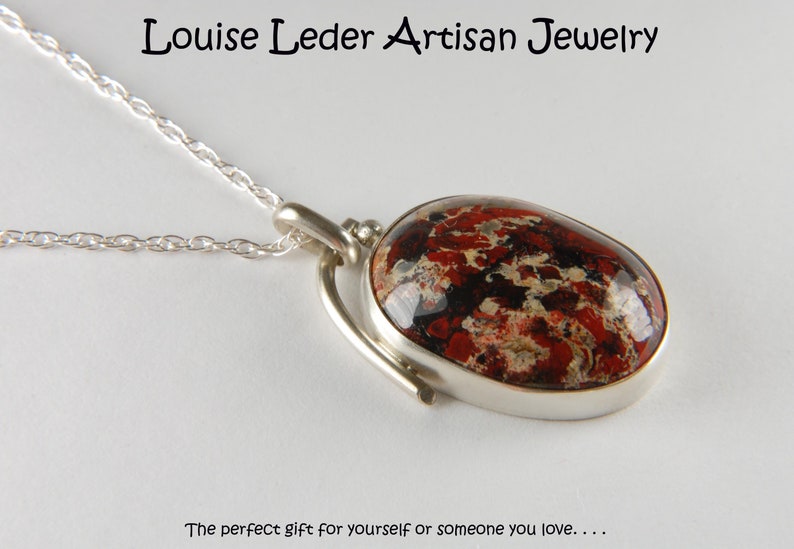 May include: A silver necklace with a red, black, and white patterned oval pendant. The pendant is set in a silver frame and hangs from a silver chain.