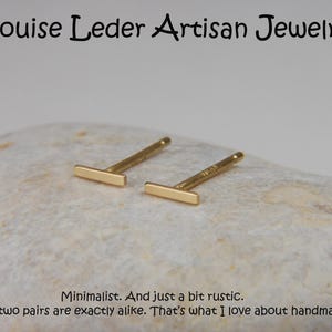 May include: A pair of gold-colored bar stud earrings. The earrings are displayed on a light-colored, textured surface. The text "Louise Leder Artisan Jewelry" is at the top. The text "Minimalist. And just a bit rustic. No two pairs are exactly alike. That's what I love about handmade!" is at the bottom.