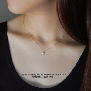 May include: A delicate gold necklace featuring a small, round pendant with a satin finish. The pendant measures 4.5 x 5 mm and hangs on a 26-inch rope chain. The necklace is shown on a person wearing a black top.