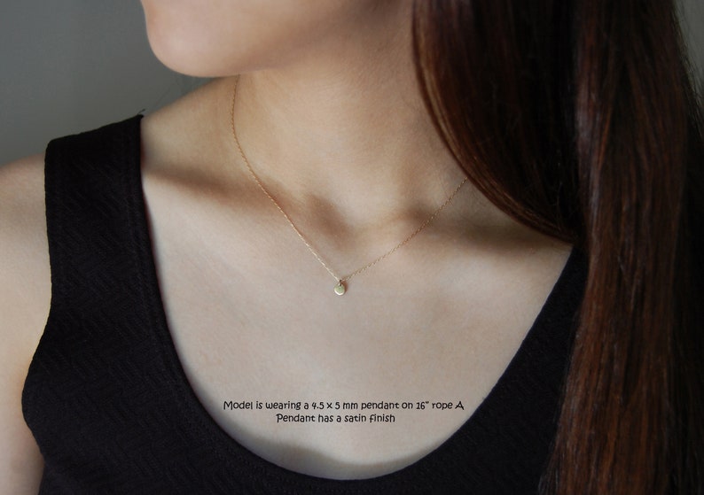 May include: A delicate gold necklace featuring a small, round pendant with a satin finish. The pendant measures 4.5 x 5 mm and hangs on a 26-inch rope chain. The necklace is shown on a person wearing a black top.