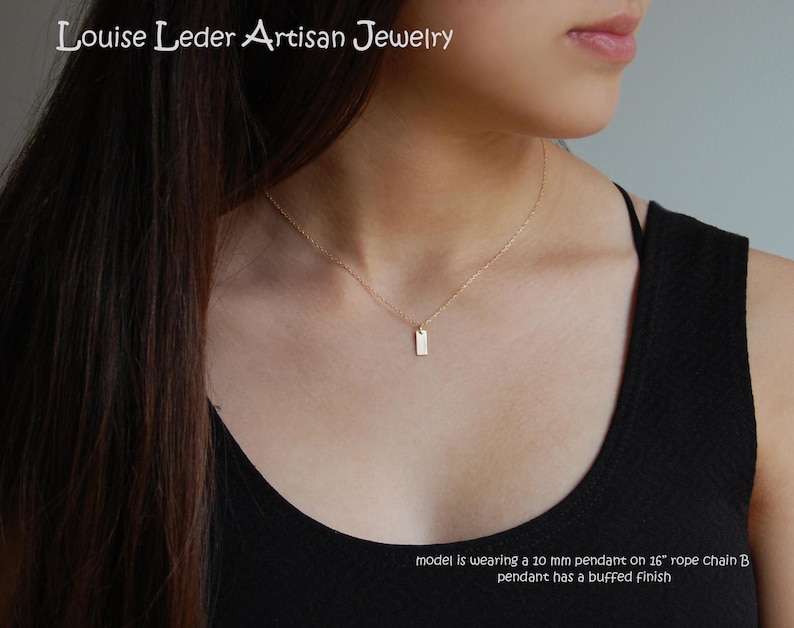 May include: A delicate gold necklace featuring a small, rectangular pendant. The pendant, approximately 10 mm in size, hangs from a thin chain. The jewelry is from Louise Leder Artisan Jewelry.
