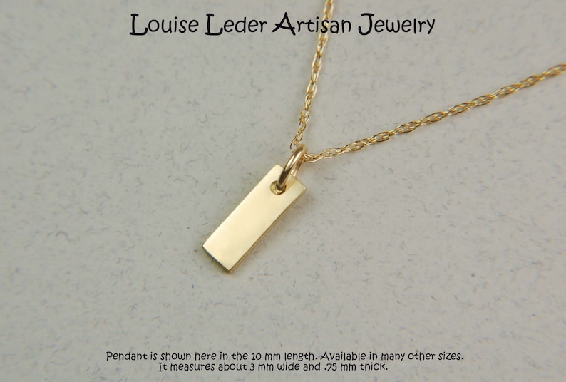 May include: A gold-coloured rectangular pendant necklace. The pendant is a small, polished rectangle suspended from a delicate chain. The necklace is from Louise Leder Artisan Jewelry. The pendant is 3 mm wide and .75 mm thick.
