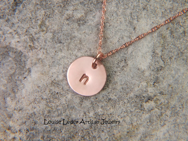 May include: A rose gold necklace featuring a small, circular pendant stamped with the lowercase letter h. The pendant hangs from a delicate, twisted chain. The text Louise Leder Artisan Jewelry is printed at the bottom of the image.